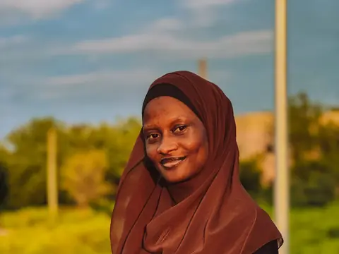 A woman in a brown hijab smiling in a sunny field