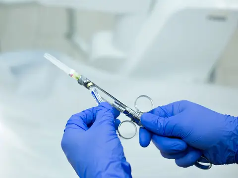 Gloved hands holding a small sterile syringe in a bright room