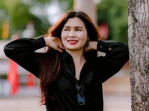 A woman laughing as she leans against a tree in a sunny park